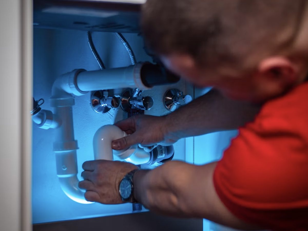 A technician working on plumbing fixtures under a sink